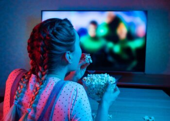 Mädchen sitzt vor dem Fernseher und isst Popcorn
