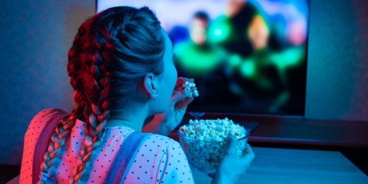 Mädchen sitzt vor dem Fernseher und isst Popcorn