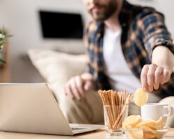 Mann sitzt am Laptop und greift zu Chips