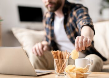 Mann sitzt am Laptop und greift zu Chips