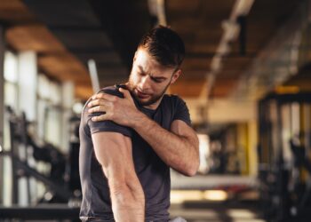 Ein Mann fasst sich in einem Fitnessstudio an die Schulter.
