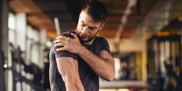 Ein Mann fasst sich in einem Fitnessstudio an die Schulter.