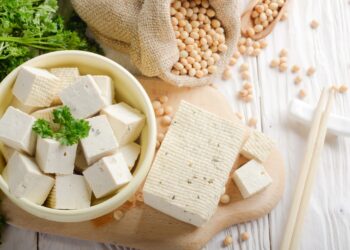 Tofu auf einem Holzbrett und in einer Schüssel neben einem Sack mit Sojabohnen