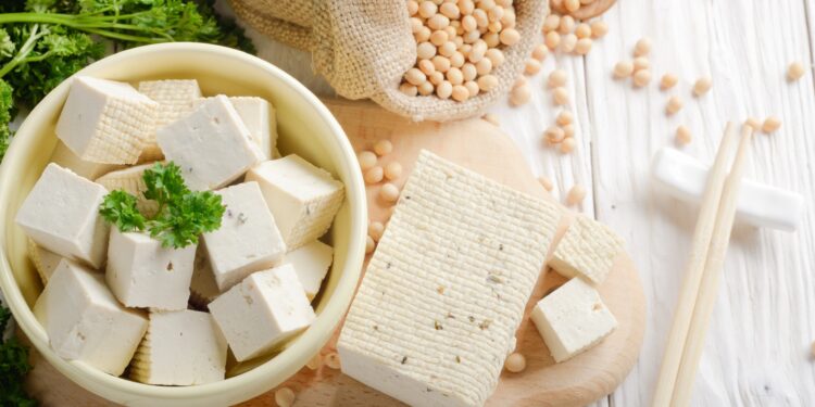 Tofu auf einem Holzbrett und in einer Schüssel neben einem Sack mit Sojabohnen