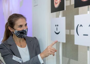 Eine Frau mit Mund-Nasenschutz steht vor einer Tafel.