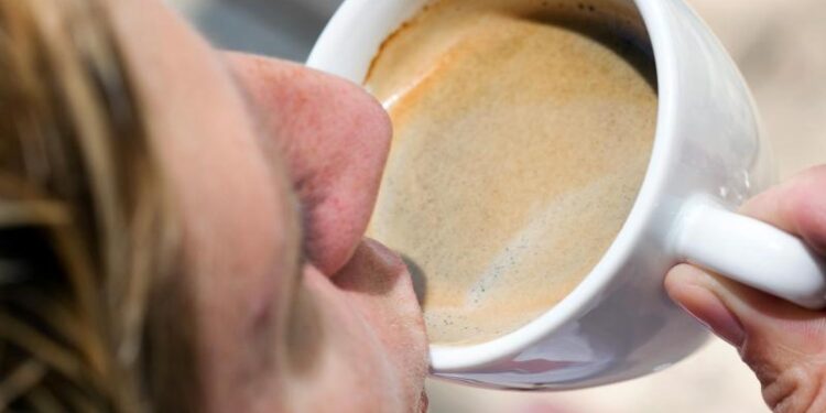 Eine Person nimmt einen Schluck Kaffee aus einer Tasse.