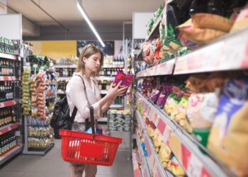 Eine junge Frau nimmt eine Packung Chips aus einem Regal im Supermarkt.