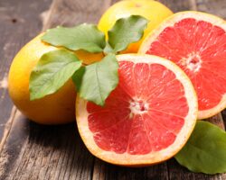 Eine halbierte und zwei weitere Grapefruits auf einem Holztisch