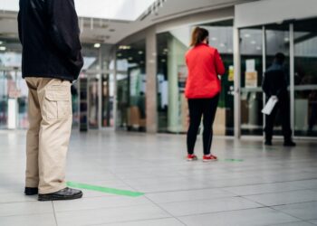 Mehrere Menschen stehen mit Abstand voneinander in einer Reihe vor einer Bank