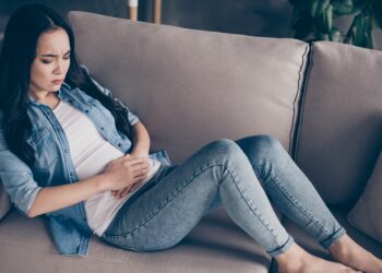 Frau sitzt auf dem Sofa und hält sich den schmerzenden Bauch.