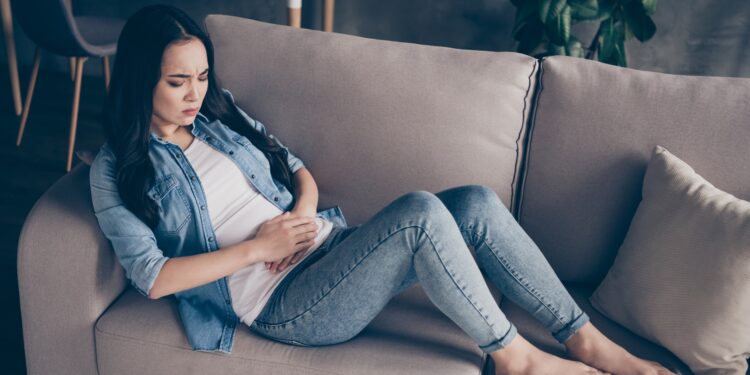 Frau sitzt auf dem Sofa und hält sich den schmerzenden Bauch.