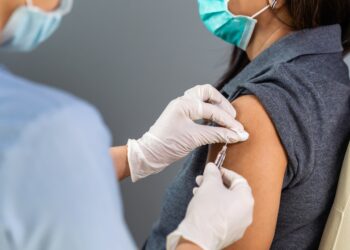 Frau mit Mund-Nasen-Bedeckung wird in den Arm geimpft