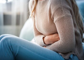 Junge Frau sitzt auf dem Sofa und hält sich ihren schmerzenden Bauch