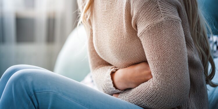 Junge Frau sitzt auf dem Sofa und hält sich ihren schmerzenden Bauch