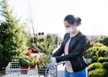 Junge Frau mit Gesichtsmaske beim Einkaufen im Freien eines Gartencenters
