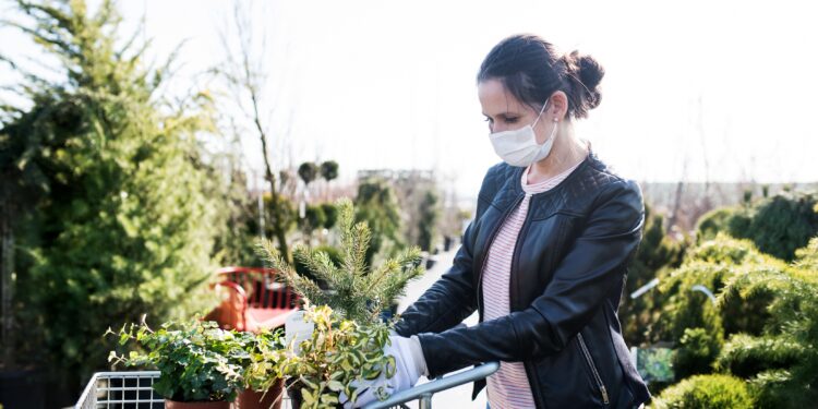 Junge Frau mit Gesichtsmaske beim Einkaufen im Freien eines Gartencenters