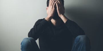 Mann sitzt auf dem Boden und bedeckt das Gesicht mit seinen Händen