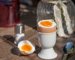 Ein Frühstücksei in einem Eierbecher sowie ein Löffel und ein Salzstreuer auf einem Tisch