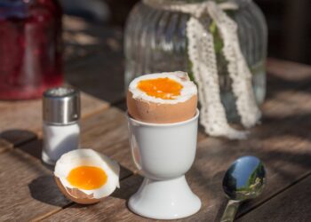 Ein Frühstücksei in einem Eierbecher sowie ein Löffel und ein Salzstreuer auf einem Tisch