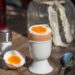 Ein Frühstücksei in einem Eierbecher sowie ein Löffel und ein Salzstreuer auf einem Tisch