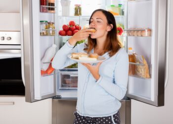 Frau verzehrt Brote vor einem Kühlschrank.