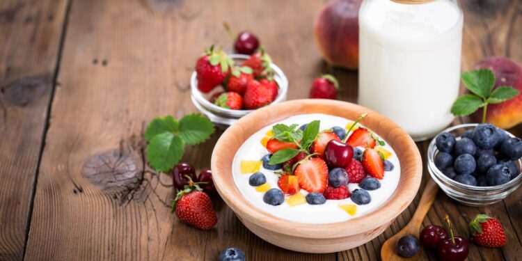 Eine Schale mit Joghurt und Früchten steht auf einer hölzernen Oberfläche.