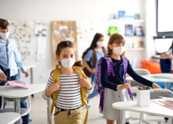 Mehrere Kinder mit Mund-Nasen-Bedeckung in einem Klassenzimmer