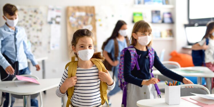 Mehrere Kinder mit Mund-Nasen-Bedeckung in einem Klassenzimmer