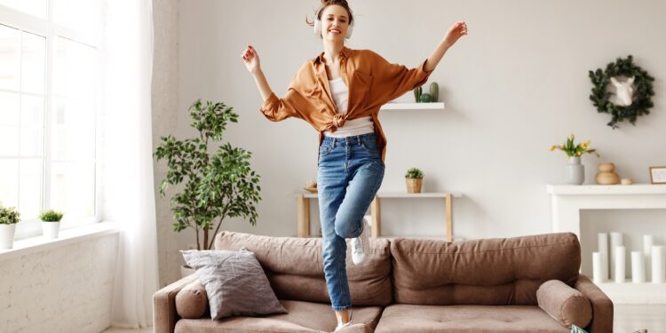 A woman listens to music and dances on the sofa.