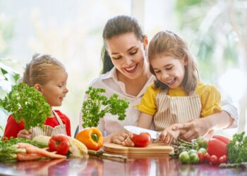 Kinder mit Mutter schneiden Obst und Gemüse.