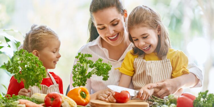 Kinder mit Mutter schneiden Obst und Gemüse.