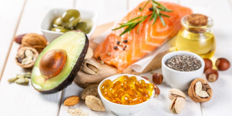 Eine Schale mit Omega-3-Präparaten steht vor gesunden Lebensmitteln, die reich an Omega-3-Fettsäuren sind.