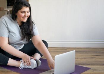 Eine übergewichtige Frau macht Fitness-Übungen vor einem Laptop.