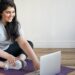 Eine übergewichtige Frau macht Fitness-Übungen vor einem Laptop.