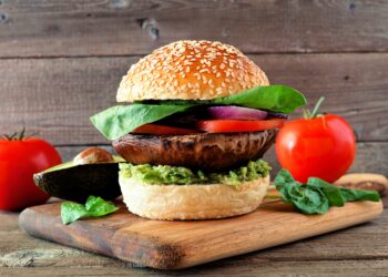 Veganer Burger mit Portobello-Pilz, Avocado, Tomate, Spinat und Zwiebeln auf einem hölzernen Servierbrett