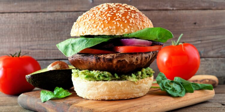 Veganer Burger mit Portobello-Pilz, Avocado, Tomate, Spinat und Zwiebeln auf einem hölzernen Servierbrett