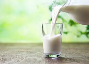 Aus einem Glaskrug wird Milch in ein Glas geschüttet