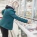 Frau mit Mund-Nasen-Bedeckung holt Ware aus der Tiefkühltruhe im Supermarkt