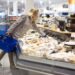 Frau im Supermarkt nimmt sich Käse aus der Selbstbedienungstheke