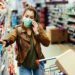 Frau mit Mund-Nasen-Bedeckung telefoniert während des Einkaufens im Supermarkt