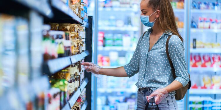 Junge Frau mit Mund-Nasen-Bedeckung beim Einkaufen im Supermarkt