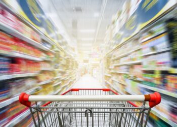 Leerer Einkaufswaagen zwischen Regalen in einem Supermarkt