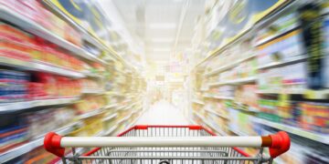 Leerer Einkaufswaagen zwischen Regalen in einem Supermarkt