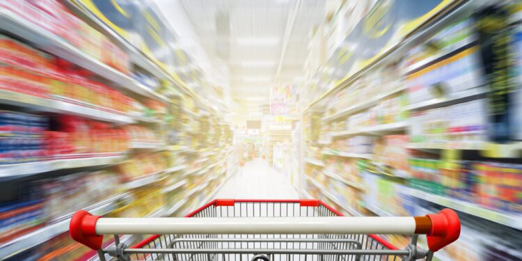 Leerer Einkaufswaagen zwischen Regalen in einem Supermarkt