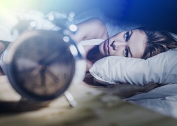 Fraue mit Schlafproblemen schaut auf die Uhr.