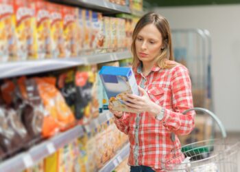 Eine Frau nimmt sich eine Packung mit Müsli aus einem Regal im Supermarkt.