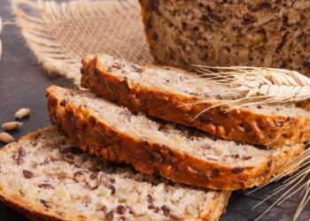 Ein zum Teil aufgeschnittenes Vollkornbrot liegt auf einer dunklen Oberfläche.