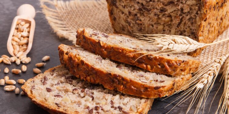 Ein zum Teil aufgeschnittenes Vollkornbrot liegt auf einer dunklen Oberfläche.