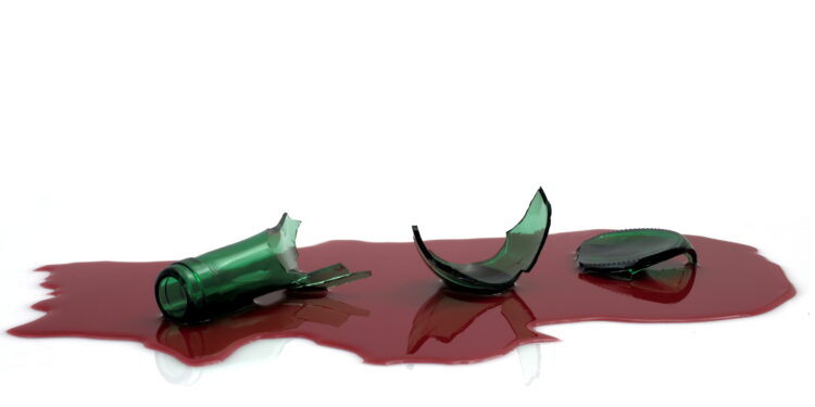 Scherben einer Weinflasche liegen in einer Lache aus roter Flüssigkeit.