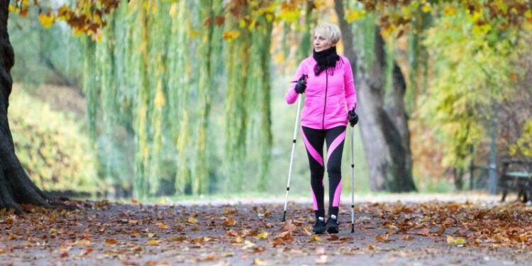 Eine Frau betreibt Nordic Walking in einer herbstlichen Landschaft.